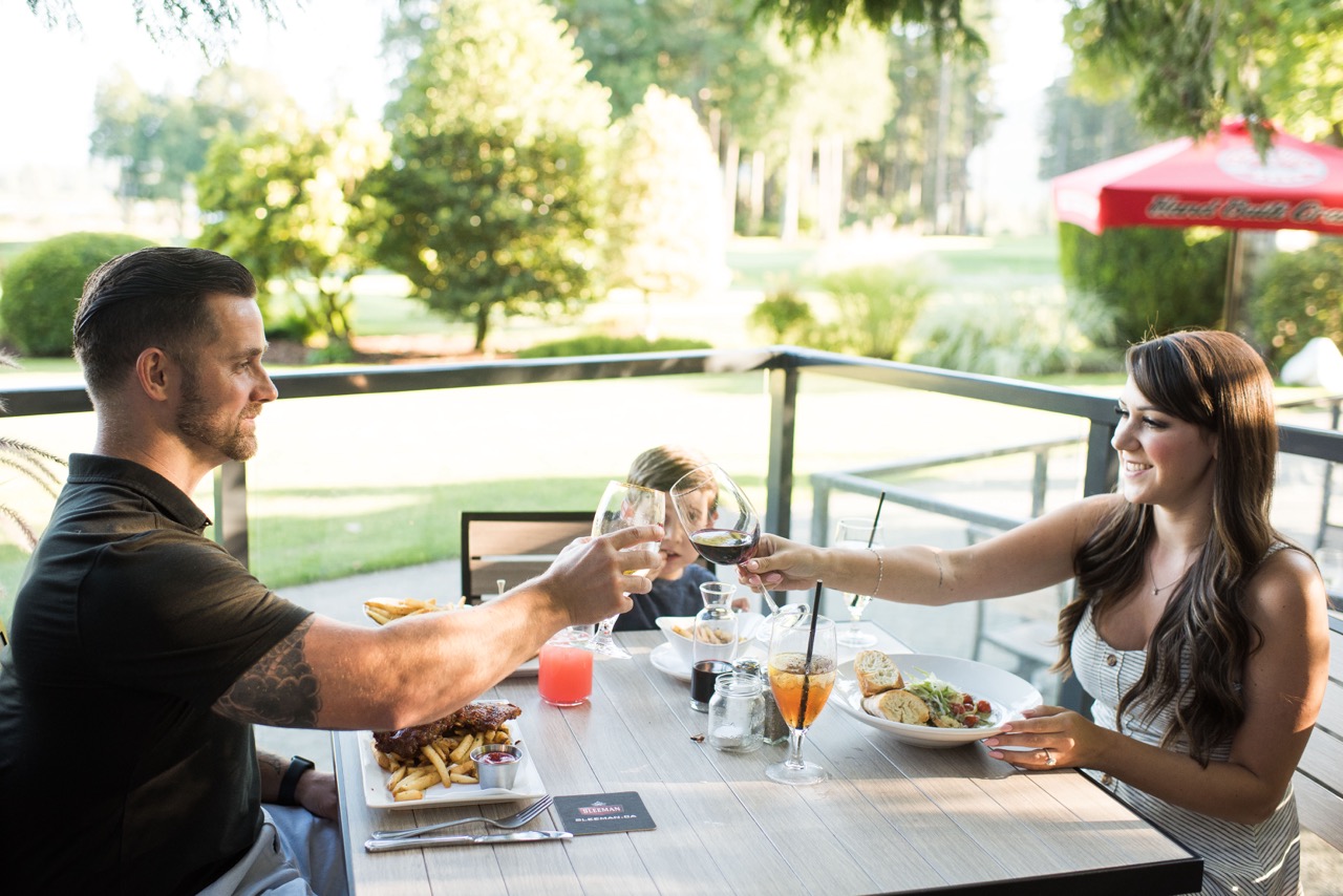 Two people sitting in an outdoor setting, having dinner and toasting their glasses of wine