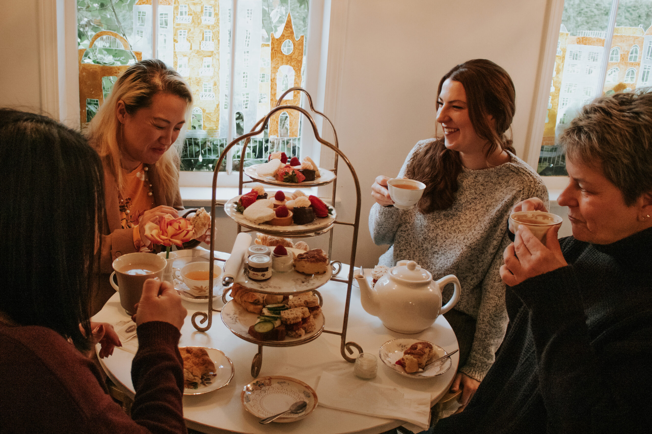Four women sit together around a table enjoying high tea.