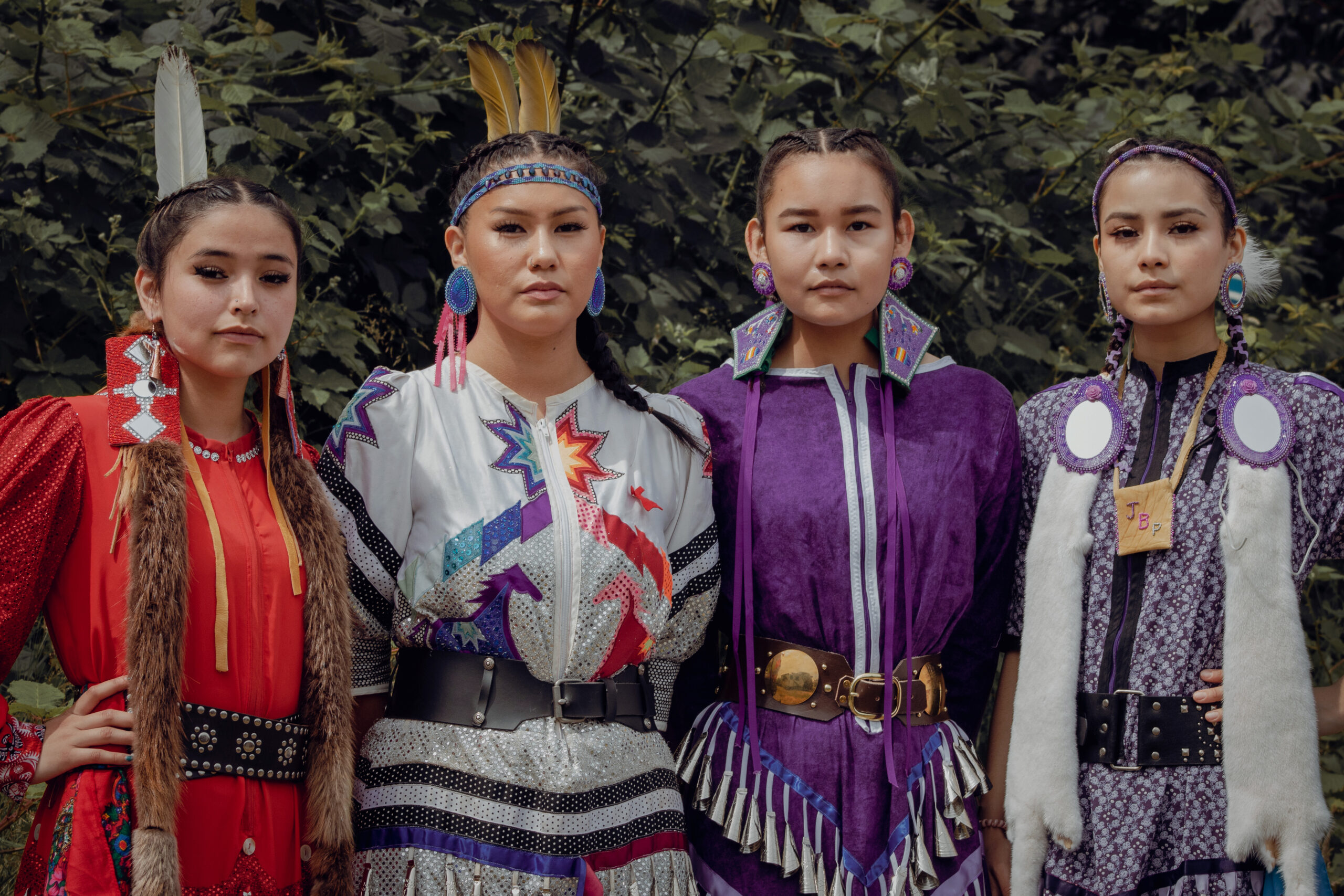 Four women wearing traditional Indigenous regalia stand together facing the camera.