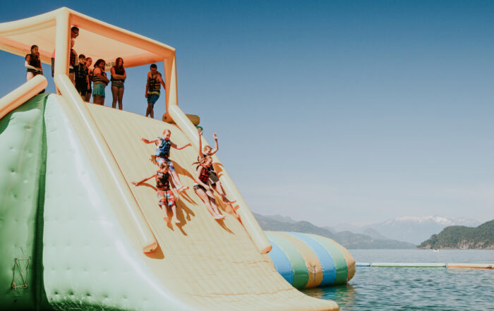 A group of young kids sliding down an inflatable slide into a lake, enjoying a summer staycation in the Valley