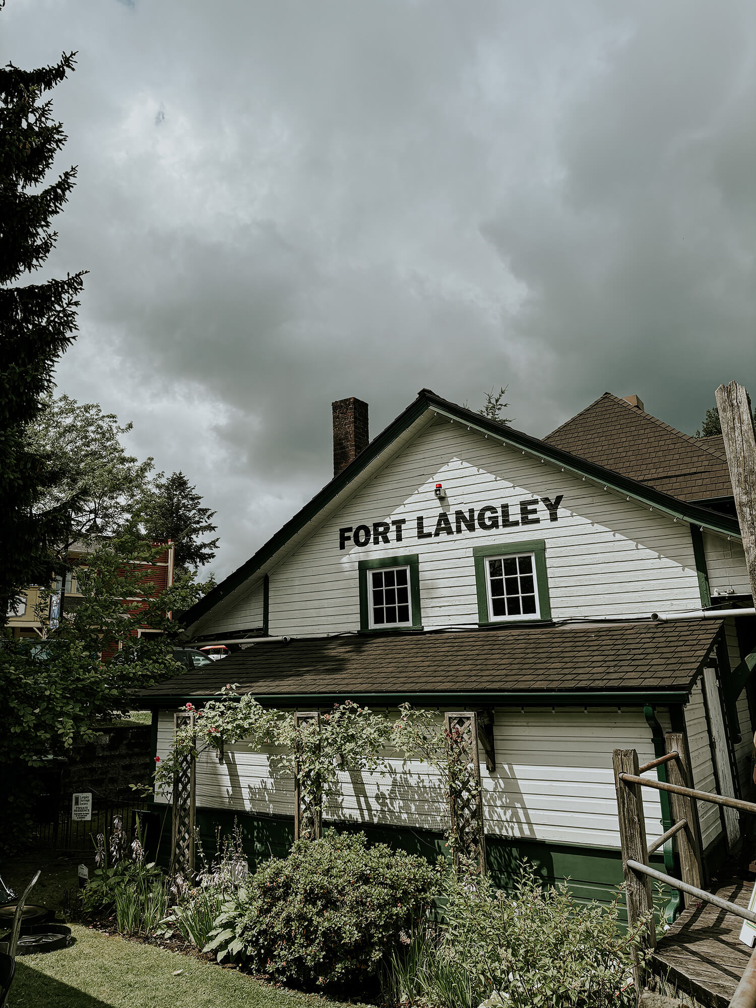 A picture of the Heritage CNR Station in Fort Langley, with bushes and trees in front and a cloudy sky