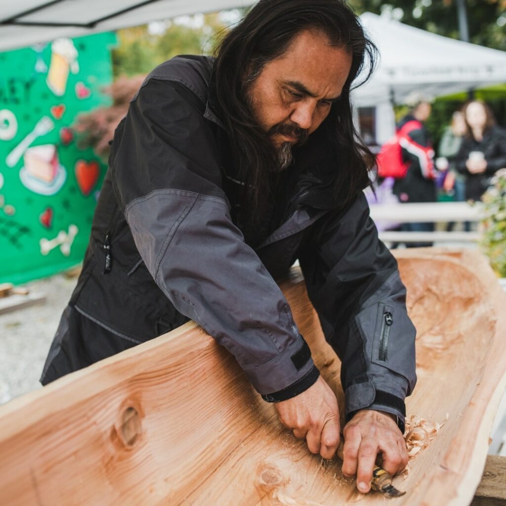 man carving wooden canoe